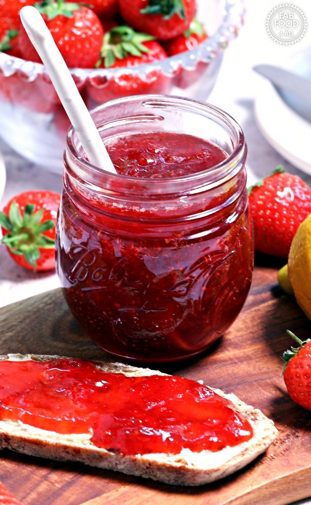 Strawberry & Gin Jam jar with spoon in it on a board with bread & jam.