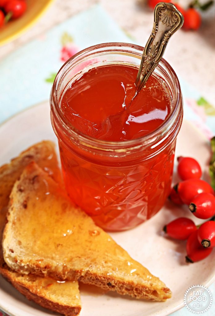 Jar of Rosehip & Apple Jelly on a plate with toast and rosehips.