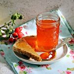 Rosehip & Apple Jelly jar on a plate with toast and teaspoon of jelly.