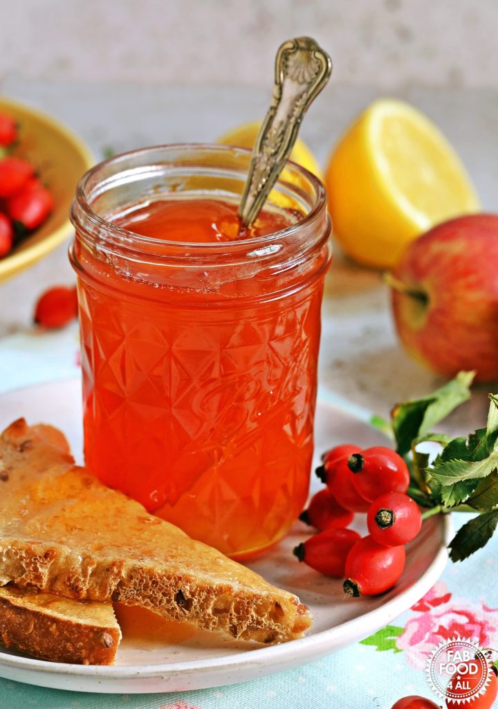 Jar of Rosehip & Apple Jelly on a plate with toast. Rosehips, apple and lemon also in shot.