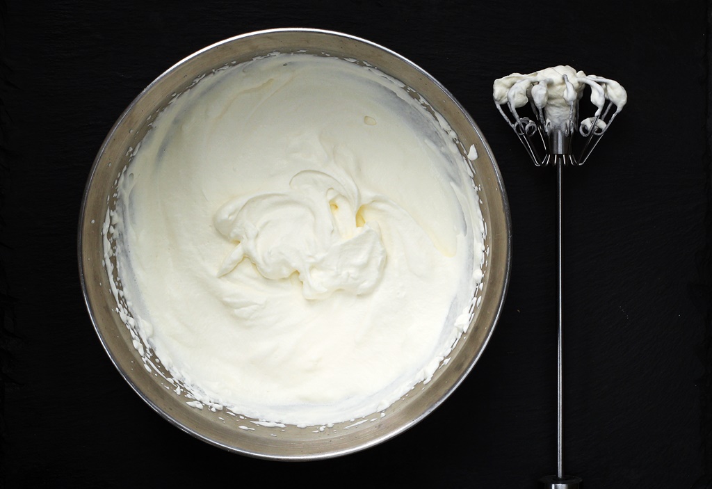 Whipped cream in a bowl with whisk.