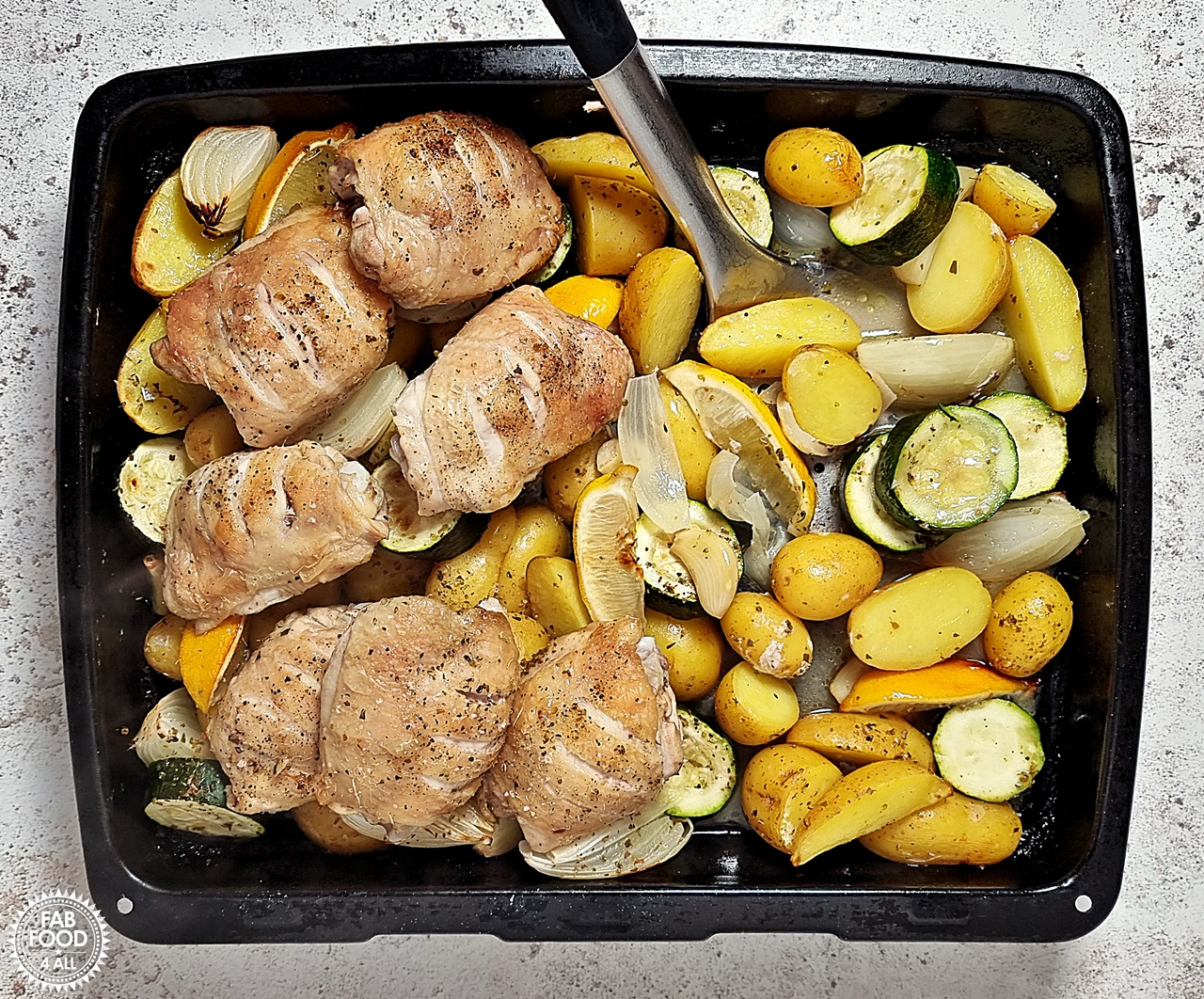 Easy Greek Chicken & Potatoes - vegetables being turned halfway through cooking with chicken thighs moved to one side.
