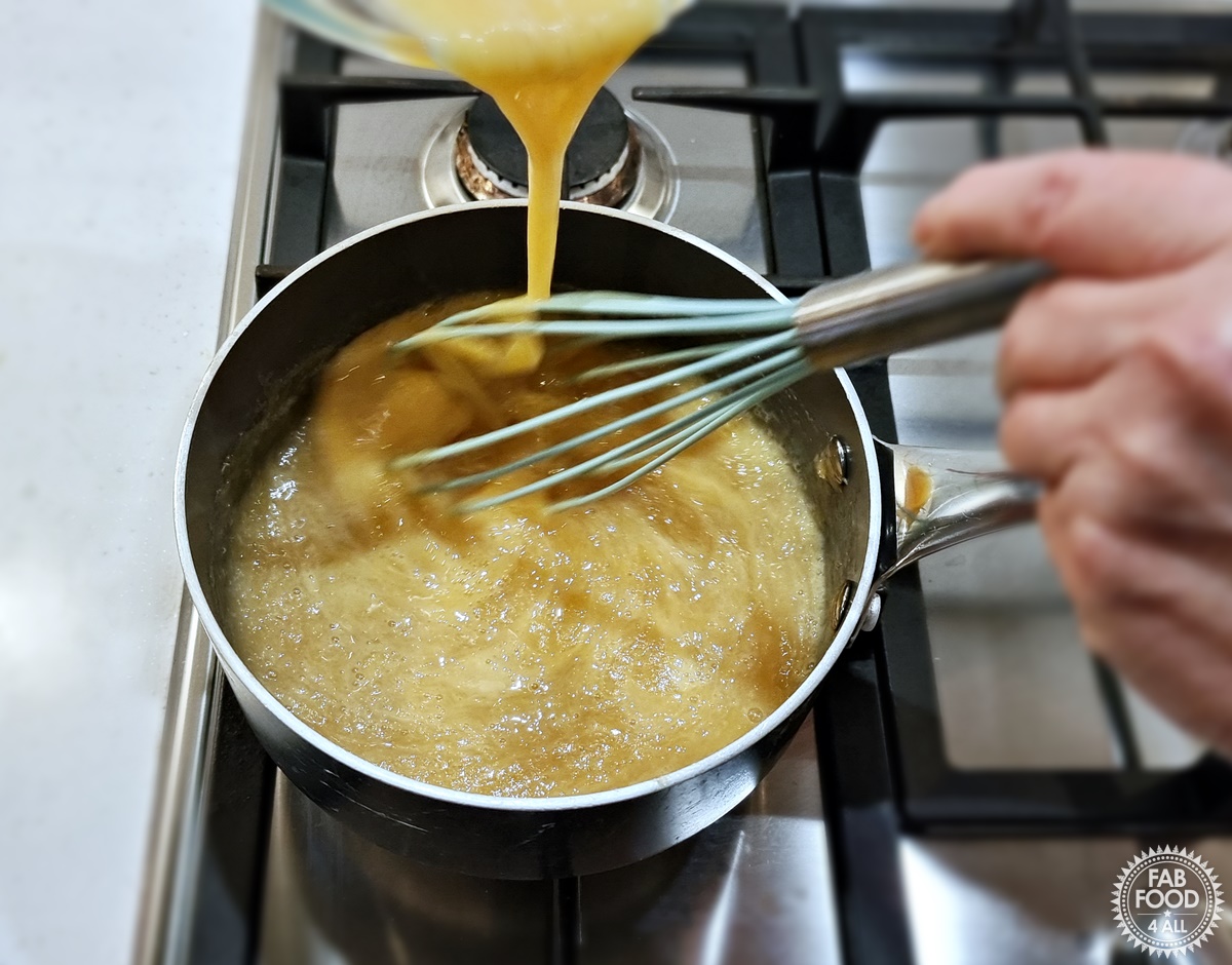 Thin stream of beaten egg being poured into pan of bubbling quince puree, sugar, butter, lemon juice and zest.