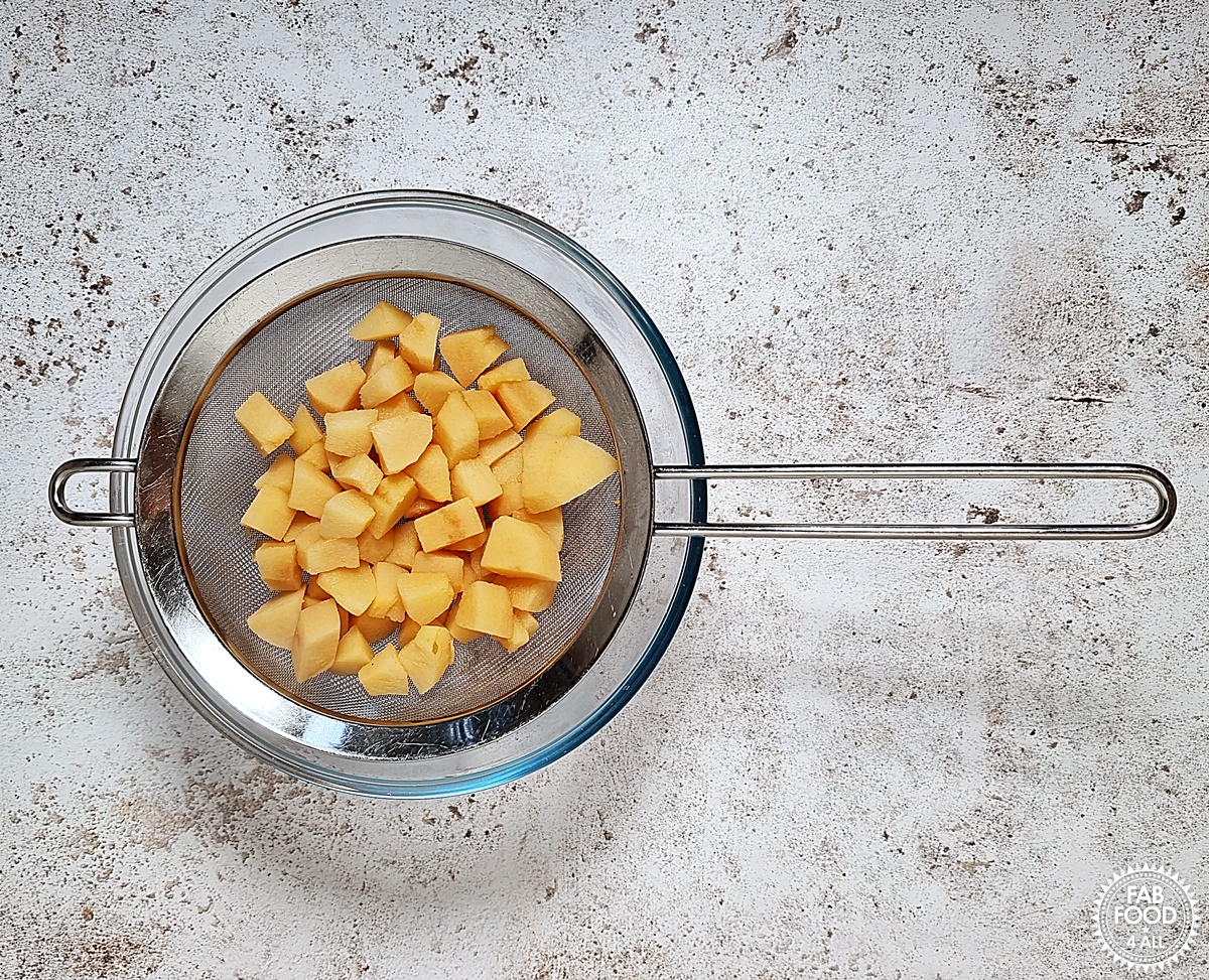 Cubed quince being drained over a bowl in a sieve.
