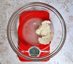 Sourdough starter and water in a bowl on digital scales.