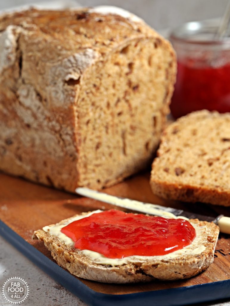 Slow Cooker Sourdough Sandwich Bread sliced and showing a slice with butter and strawberry jam.