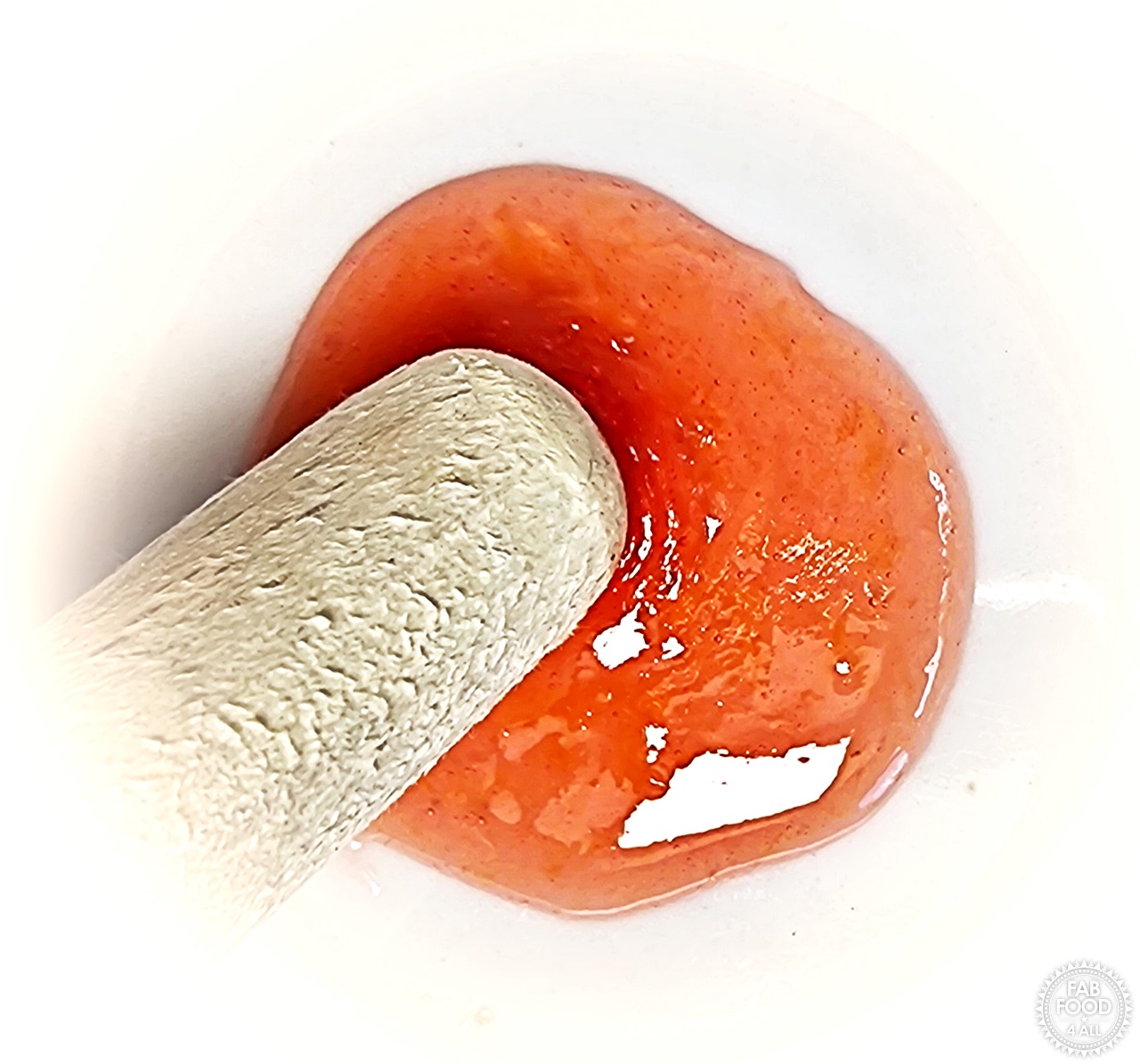 Tip of wooden spoon being pushed through a blob of jam on a chilled saucer showing subtle crinkles to test for set.