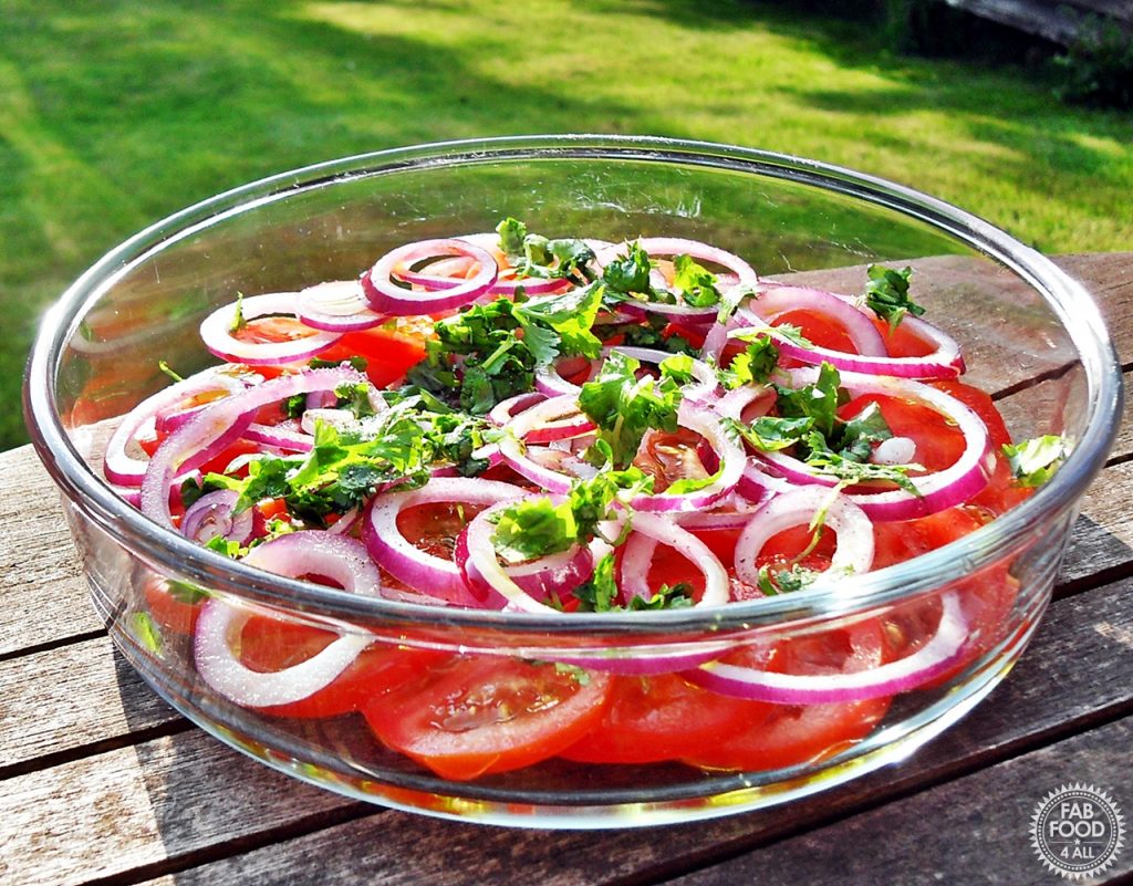 Tomato, Red Onion and Coriander Salad in a shallow, round glass Pyrex dish on a garden table with lawn in background.