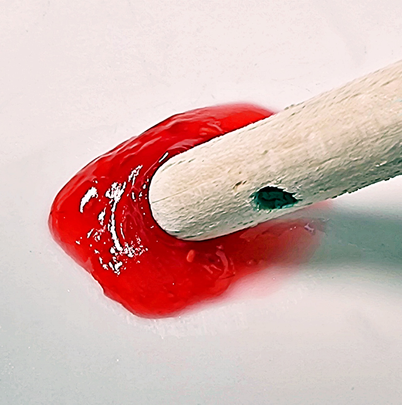 Tip of a wooden spoon being pushed through a few drops of jam on chilled plate showing it crinkling up ie at setting point.