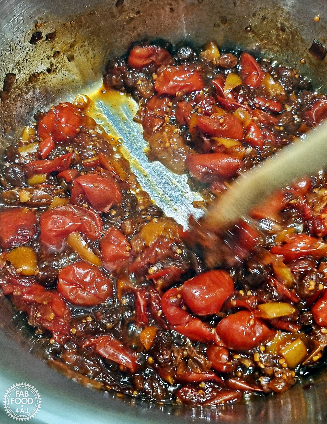 Spicy Baby Tomato & Sweet Pepper Chutney in a pan showing a wooden spoon parting the chutney in the base of the pan to show it's ready.