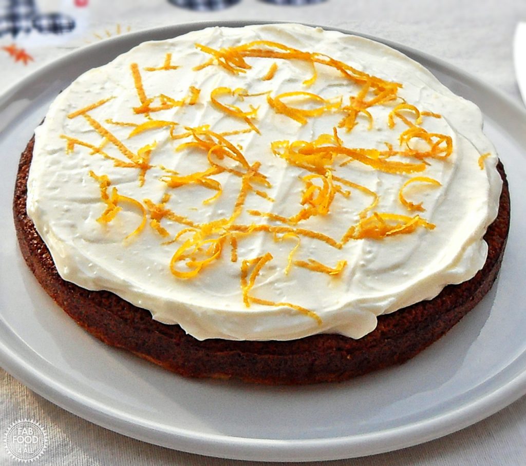 Quick & Easy Spelt Butternut Squash Cake with orange cream cheese frosting decorated in orange skin shavings on a white serving dish.