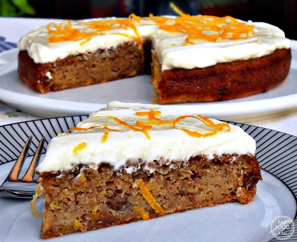 Quick & Easy Spelt Butternut Squash Cake with orange cream cheese icing decorated in orange zest shavings on a white serving dish with slice on a plate in the foreground.