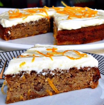 Quick & Easy Spelt Butternut Squash Cake with orange cream cheese icing decorated in orange zest shavings on a white serving dish with slice on a plate in the foreground.