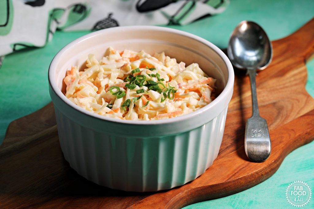Landscape shot of Easy Classic Coleslaw in a bowl on a board with serving spoon.