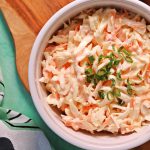 Bowl of Easy Classic Coleslaw on a wooden board with serving spoon (overhead view).