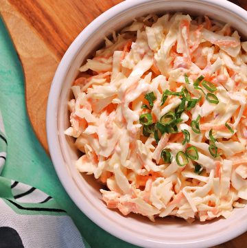 Bowl of Easy Classic Coleslaw on a wooden board with serving spoon (overhead view).