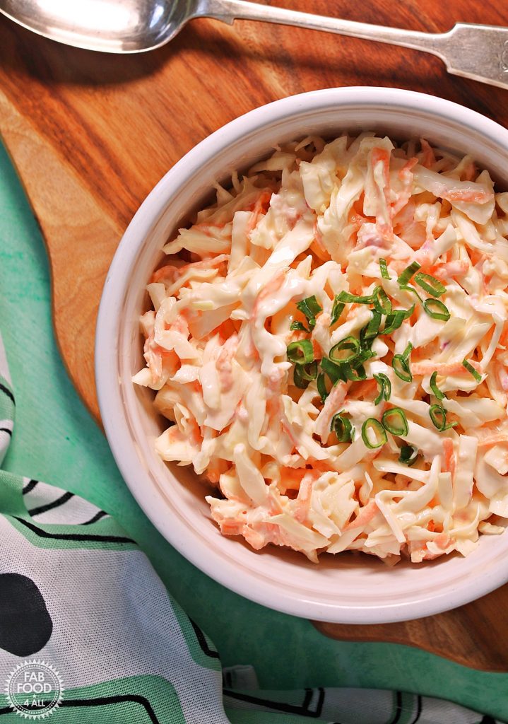 Bowl of Easy Classic Coleslaw on a wooden board with serving spoon (overhead view).