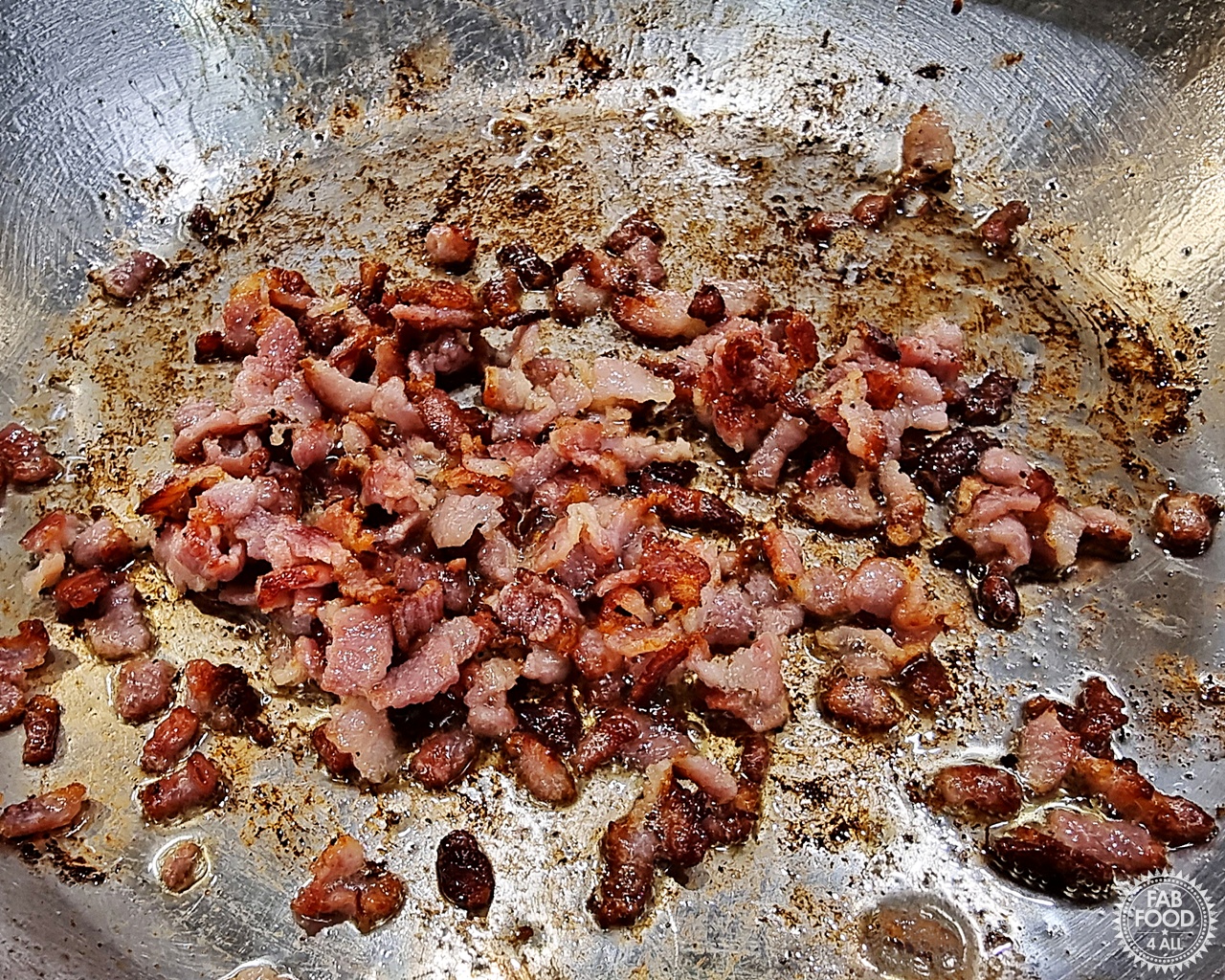 Chopped bacon frying in a pan.