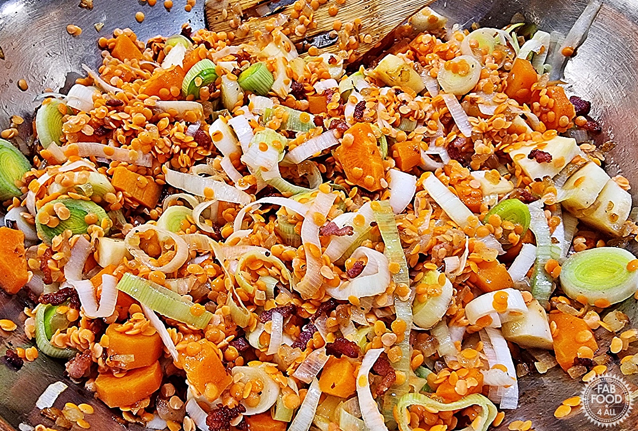 Red lentils, fried onion and bacon added to the chopped carrots, parsnip and leeks in a pan.