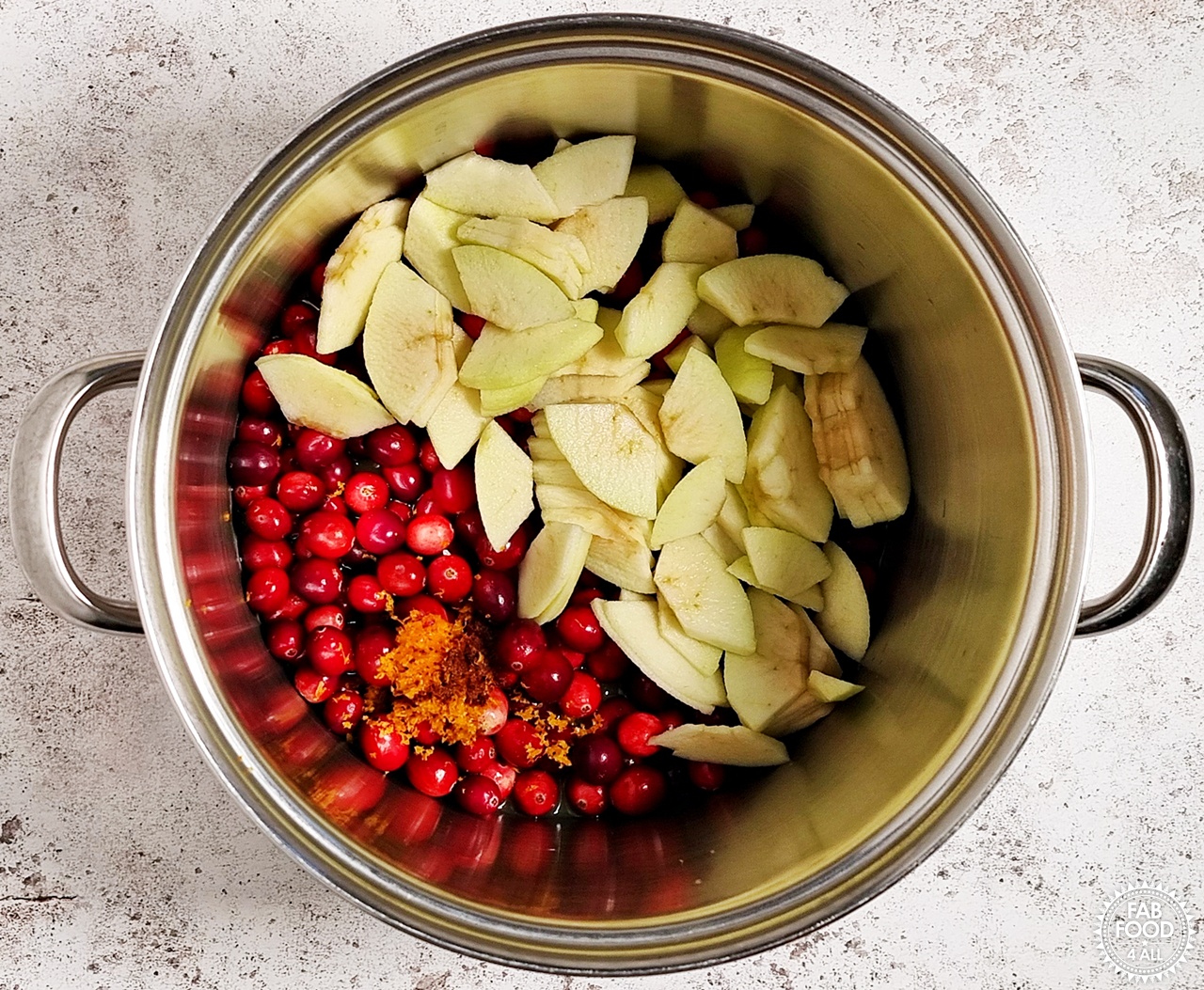 Deep stainless steel pan with Easy Christmas Jam ingredients: cranberries, cored, peeled and sliced cooking apples, orange juice, orange zest and mixed spice.