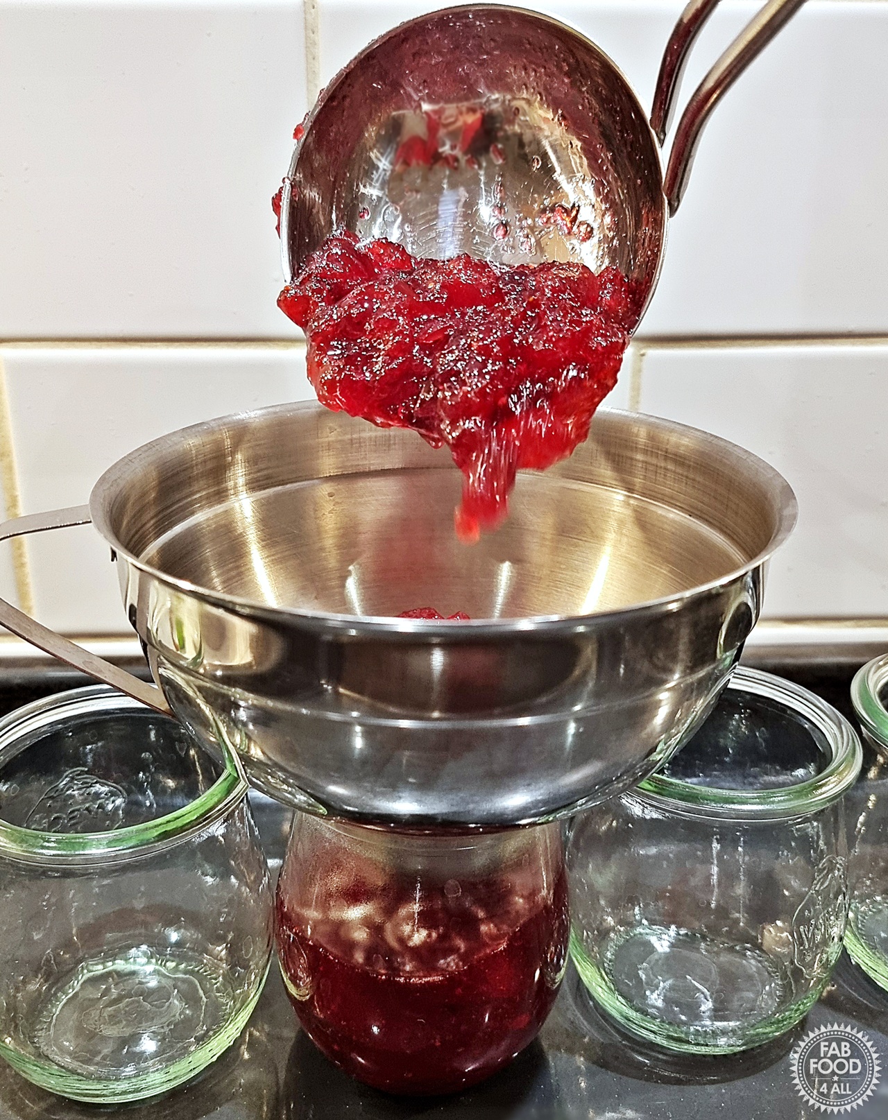 Easy Christmas Jam being ladled into a jar with a jam funnel on top.