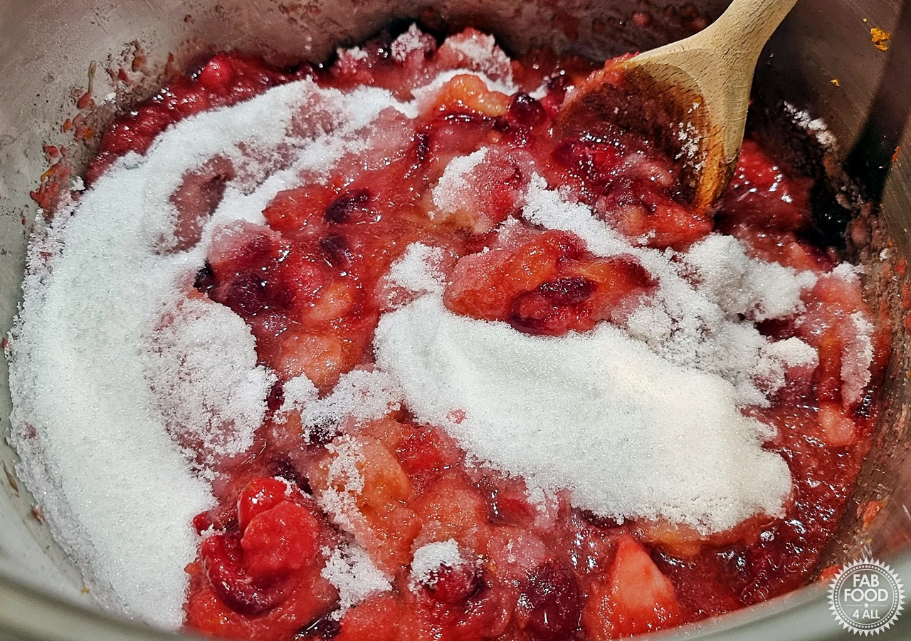 Granulated sugar being stirred into simmered cranberry and apple mixture.
