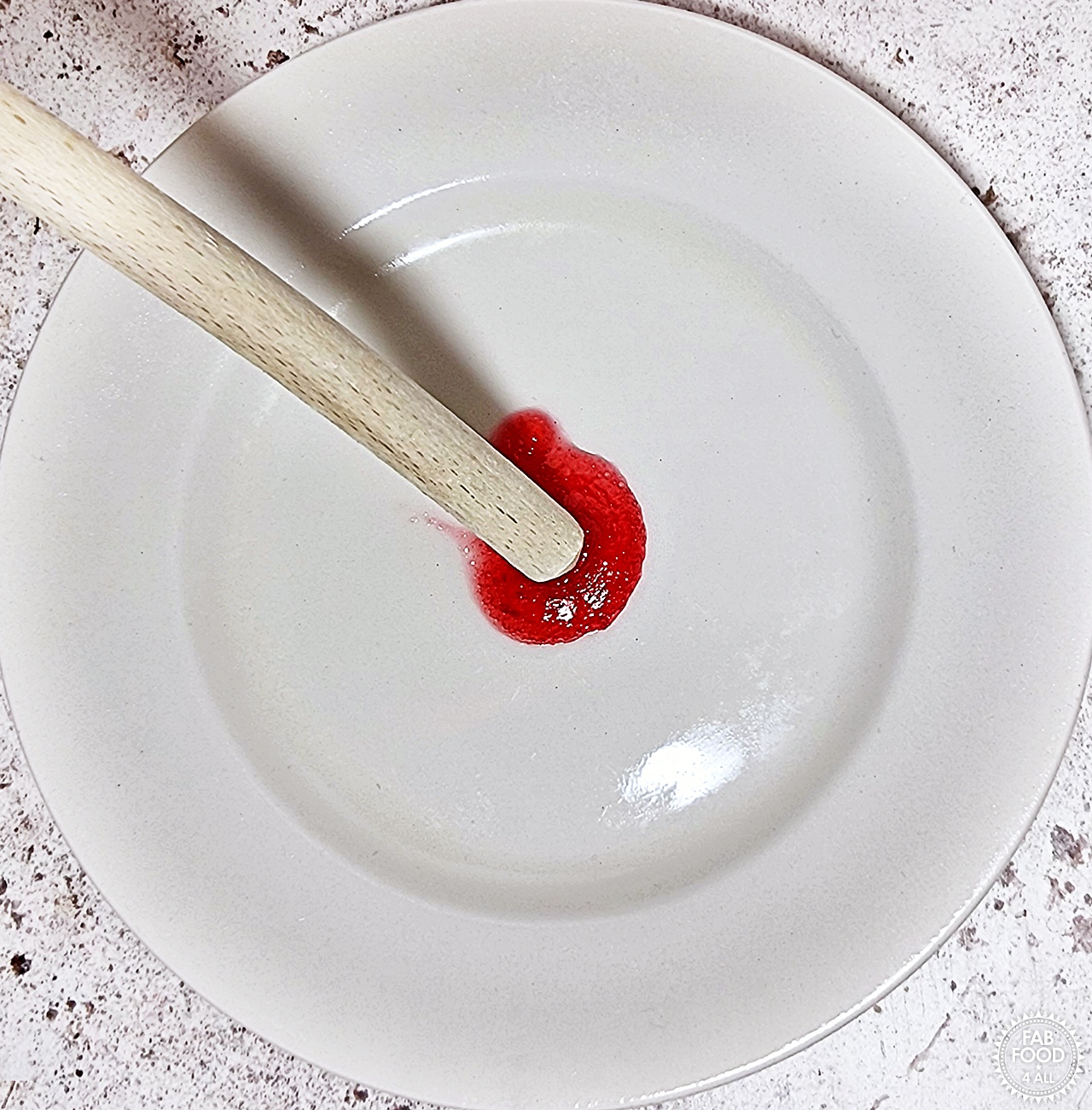 The handle of a wooden spoon being pushed through a blob of Easy Christmas Jam showing the crinkle that indicates it has reached setting point.