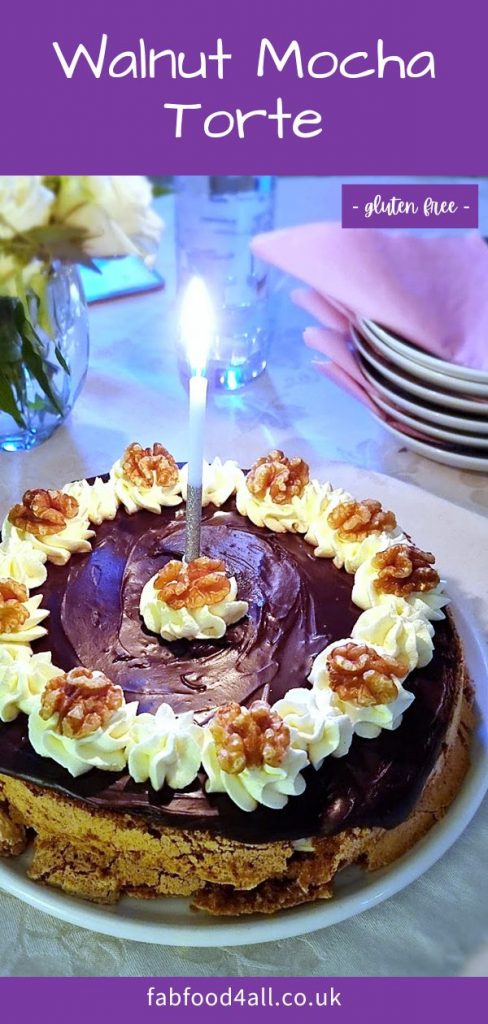 Walnut Mocha Torte on a platter with lit birthday candle. Plates, napkins and a vase of flowers in the background. Pinterest image.