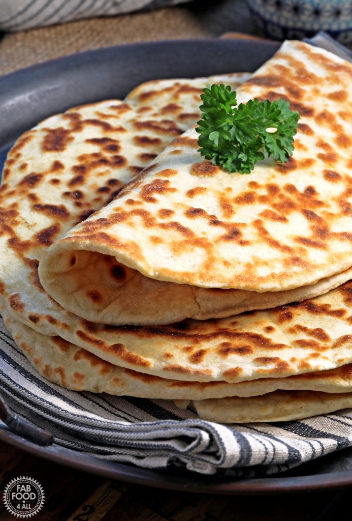 Close up of a stack of Easy Spelt Yogurt Flatbreads with top one folded over and topped with a sprig of parsley.