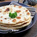 Stack of Easy Spelt Yogurt Flatbreads on a tin platter garnished with a sprig of parsley. Showing spotty side.