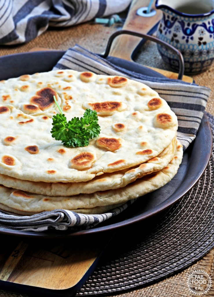 Stack of Easy Spelt Yogurt Flatbreads on a tin platter garnished with a sprig of parsley. Showing spotty side.