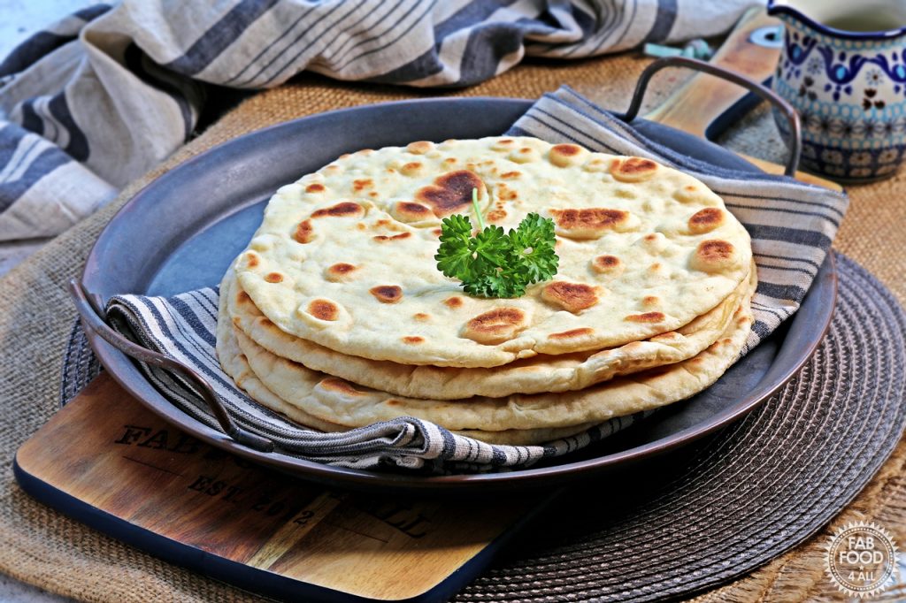 Stack of 4 easy spelt yogurt flatbreads topped with a sprig of parsley. Spotty side on display.