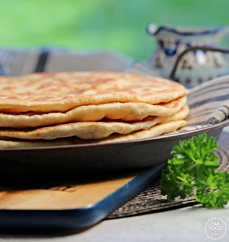 Stack of 4 Easy Spelt Yogurt Flatbreads on a cloth on a tin dish in front of a window.