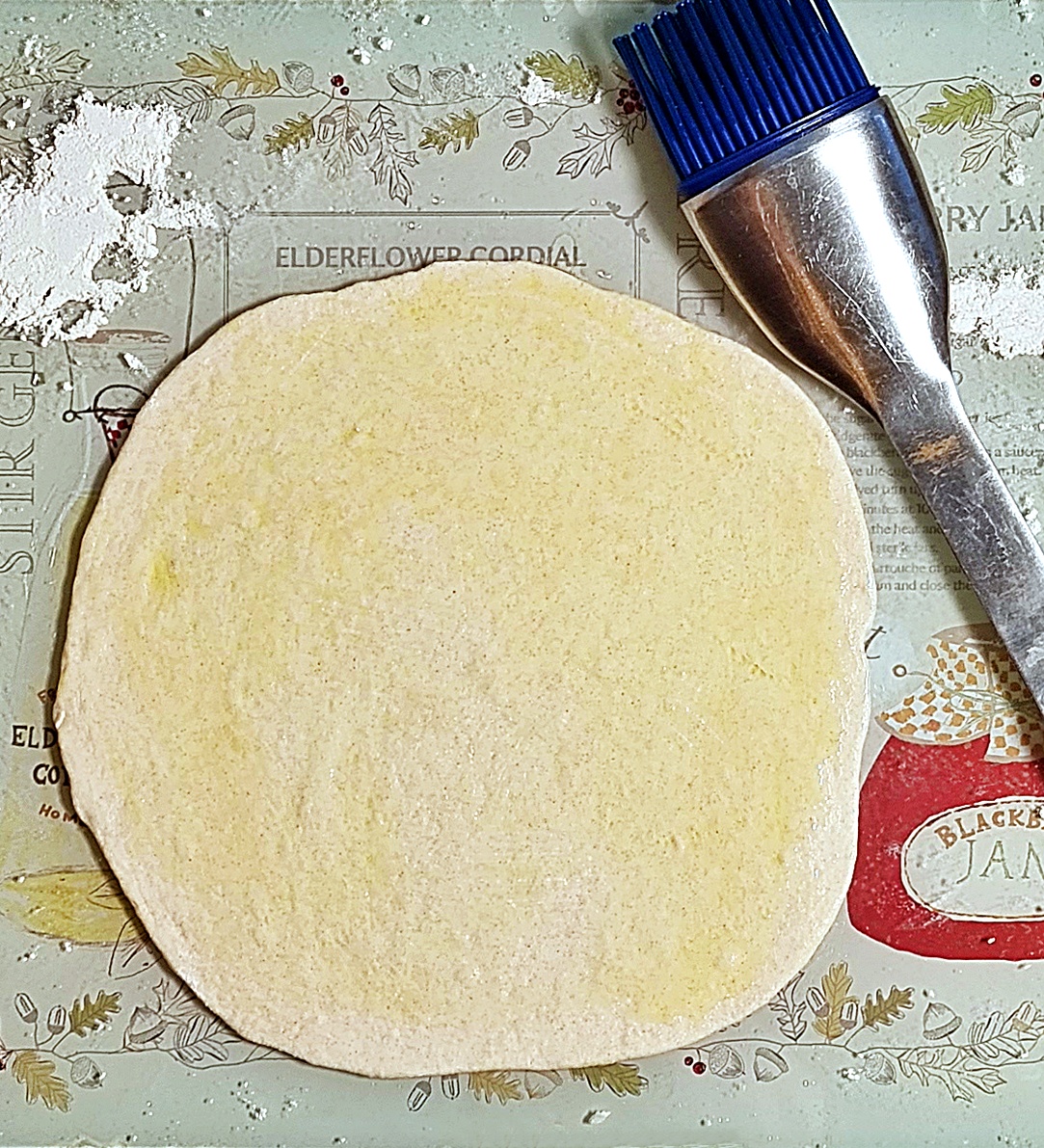 Rolled out Spelt Yogurt Flatbread dough that has been brushed with extra virgin olive oil. Silicone pastry brush top right.