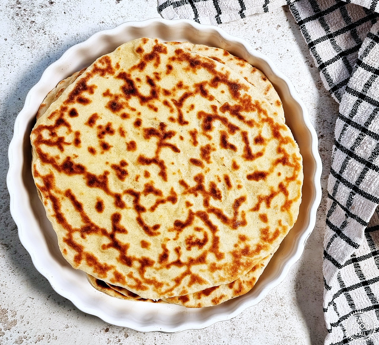 Cooked flatbreads in a dish with a tea towel next to it.