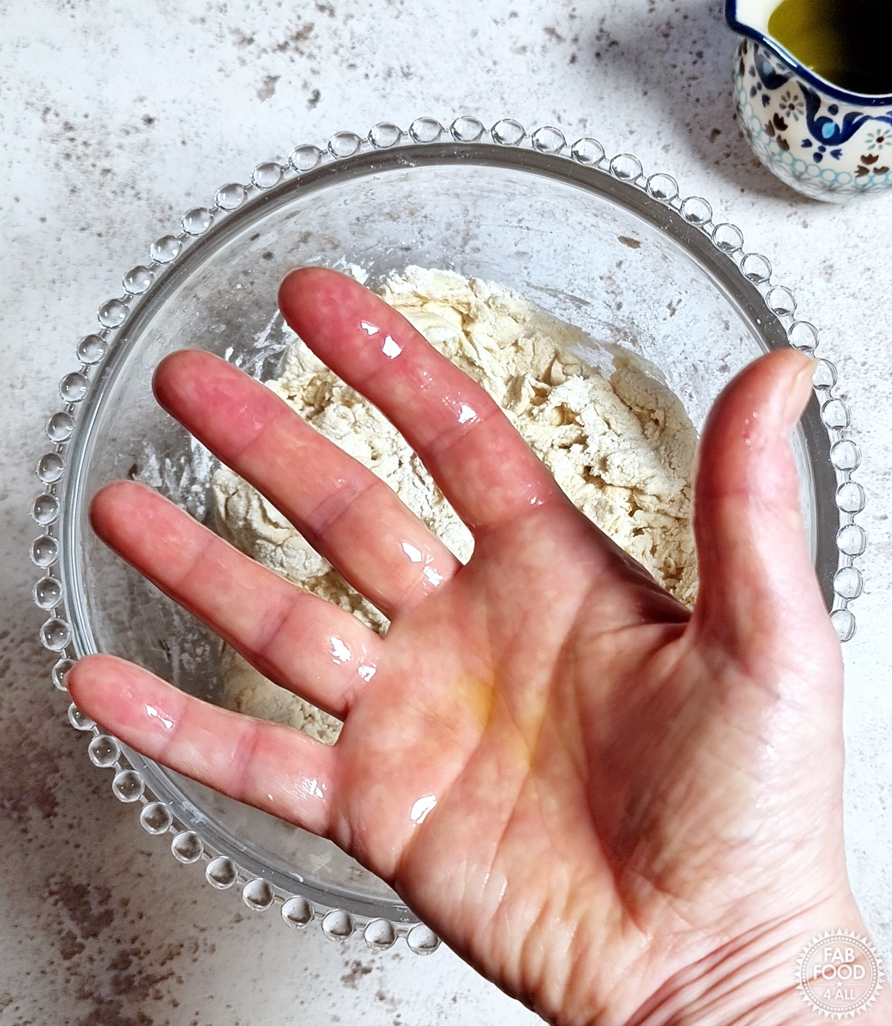 Oiled hand above a bowl of flatbread dough.