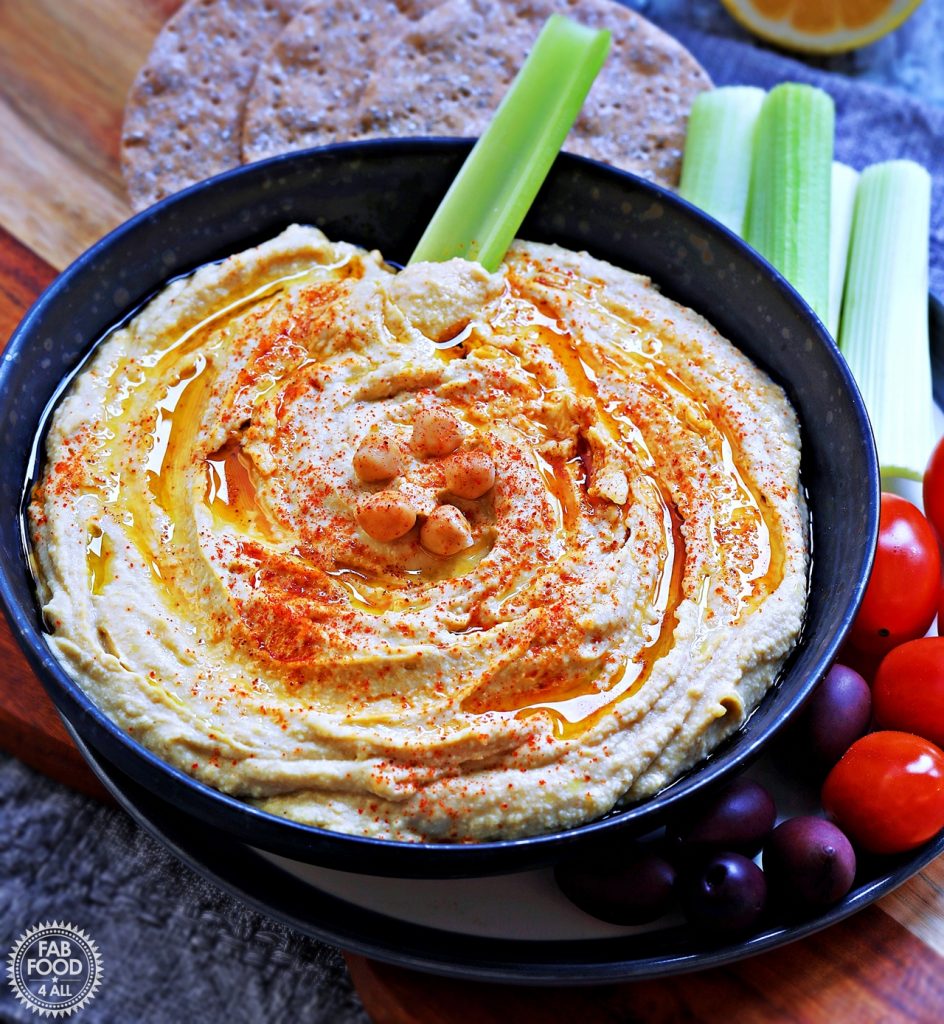 Bowl of hummus with a stick of celery in it (surrounded by crudités and crackers).