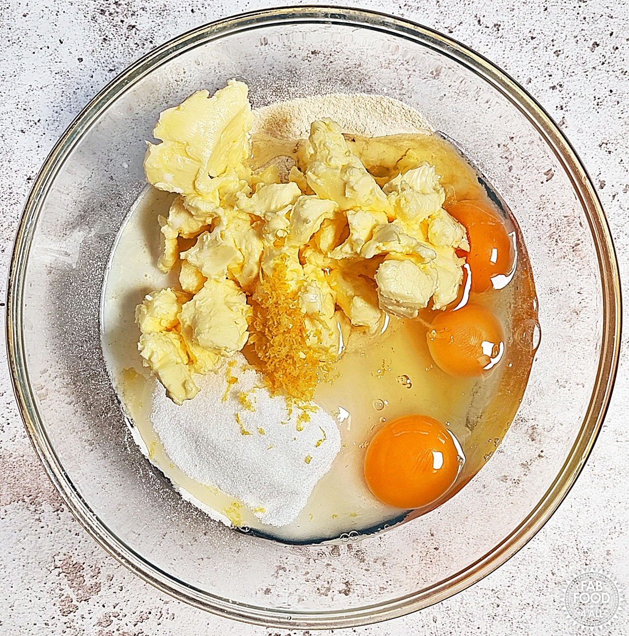 Bowl of sifted flour and baking powder, caster sugar, butter, eggs, zest of a lemon and milk.