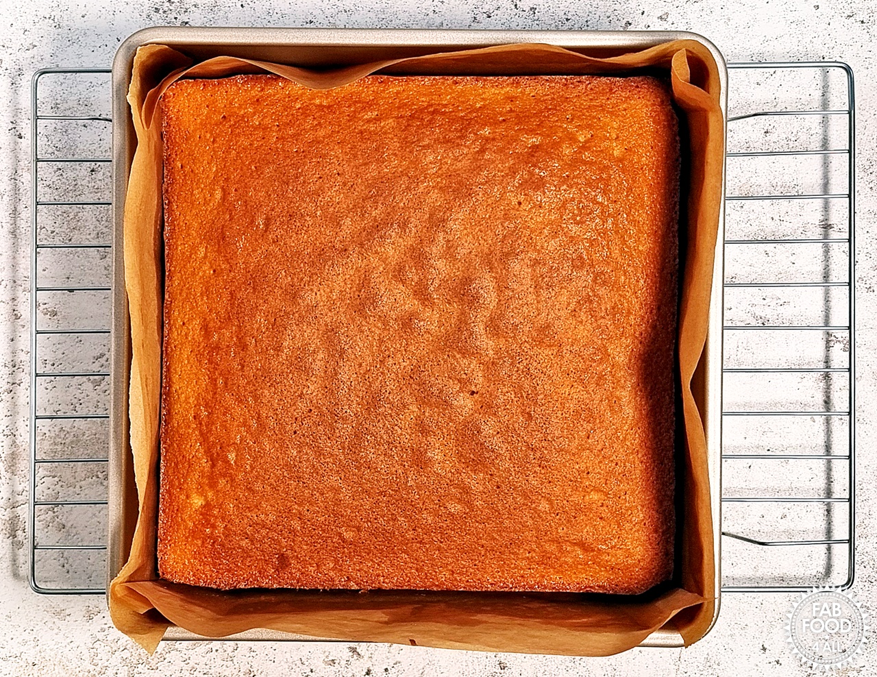 Lemon Drizzle Traybake cooling in tin on a wire rack for a few minutes.