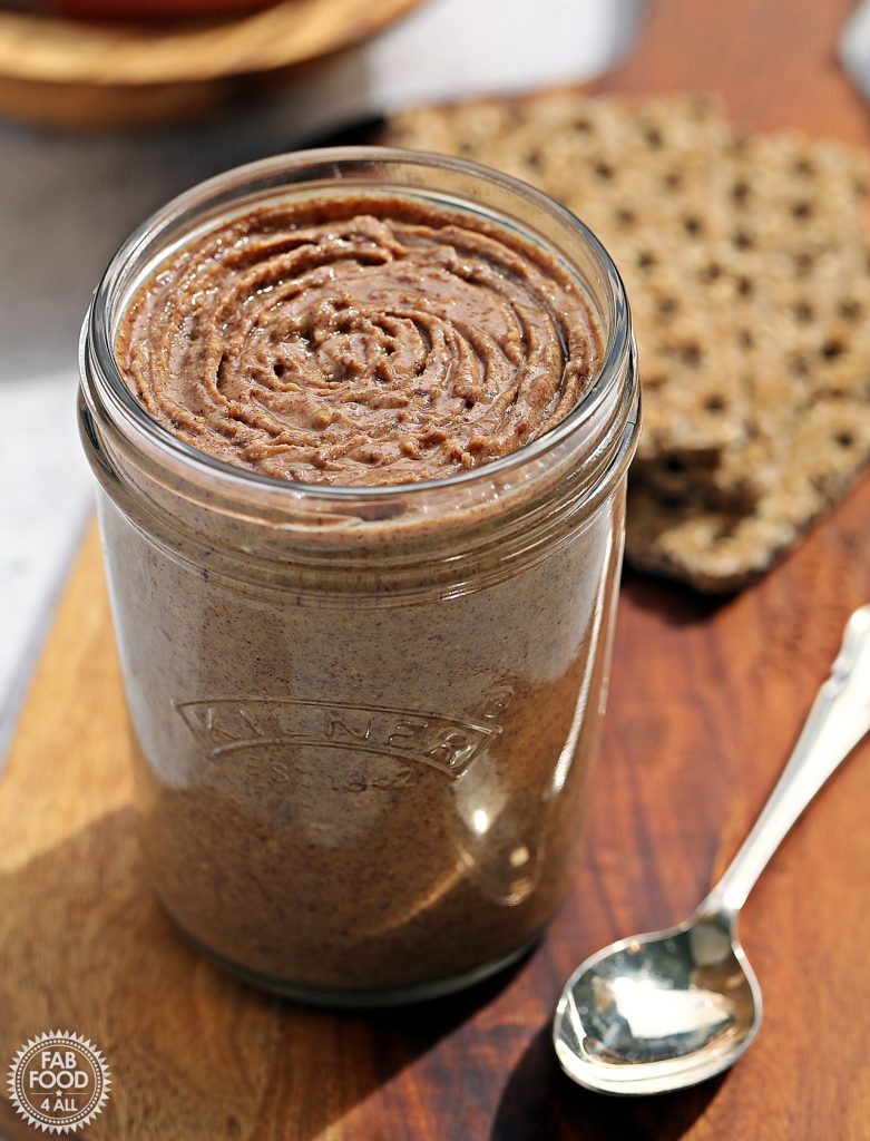 Homemade Peanut Butter on a board with silver teaspoon and crackers in the background.