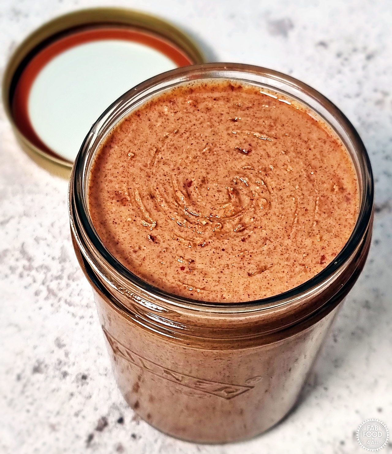 Homemade peanut butter in a jar with lid in background.