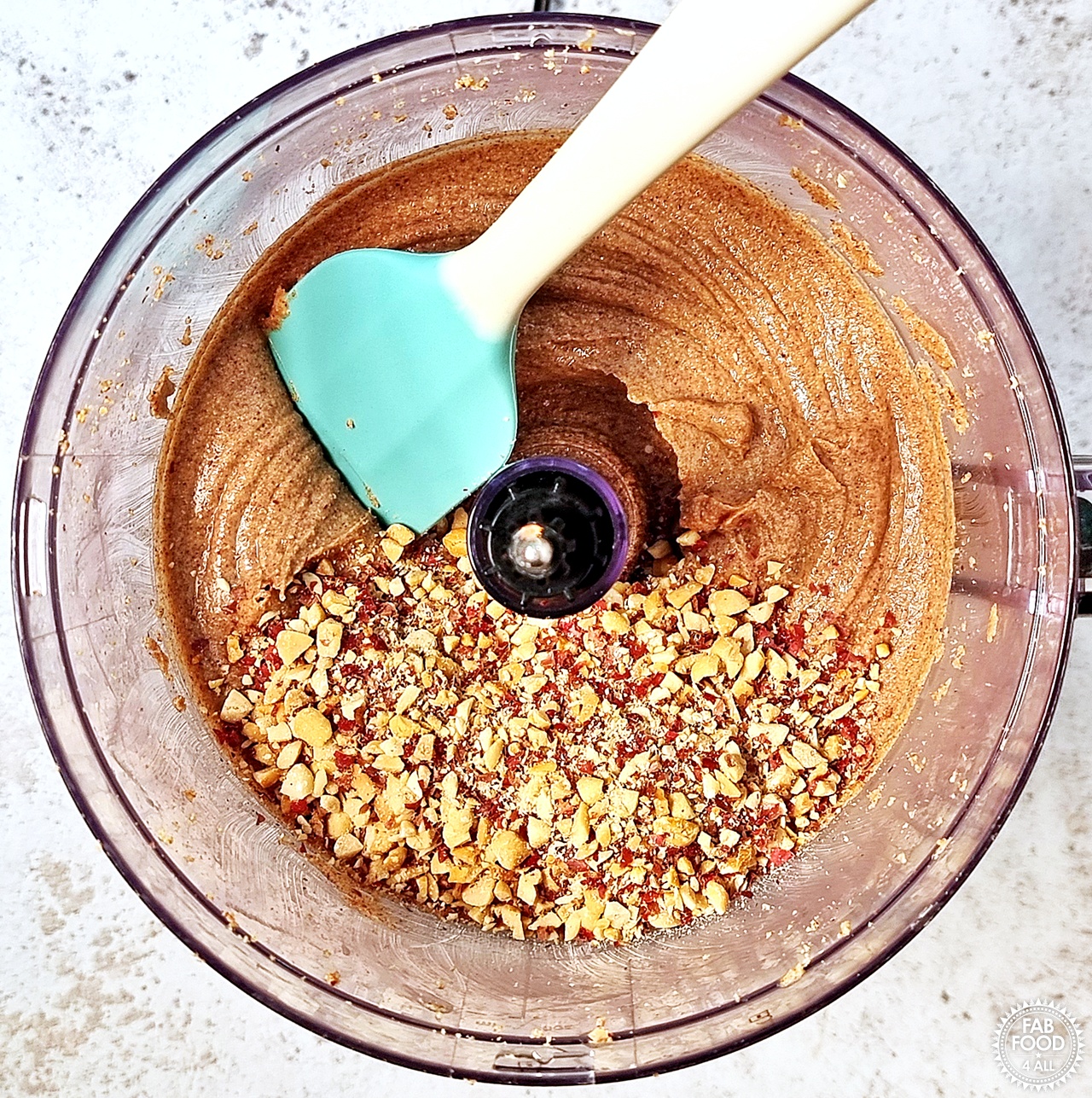 Chopped nuts that were removed added back to the peanut butter (optional). Spatula ready to mix in. Blade has been removed from food processor.