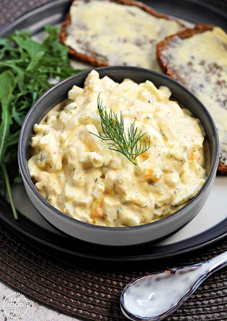 Healthy Egg Salad with Greek Yogurt (No Mayo) in a bowl with rocket and buttered rye bread on a plate.