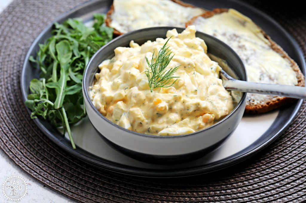 Healthy Egg Salad with Greek Yogurt (No Mayo) in a bowl with rocket and buttered rye bread on a plate.
