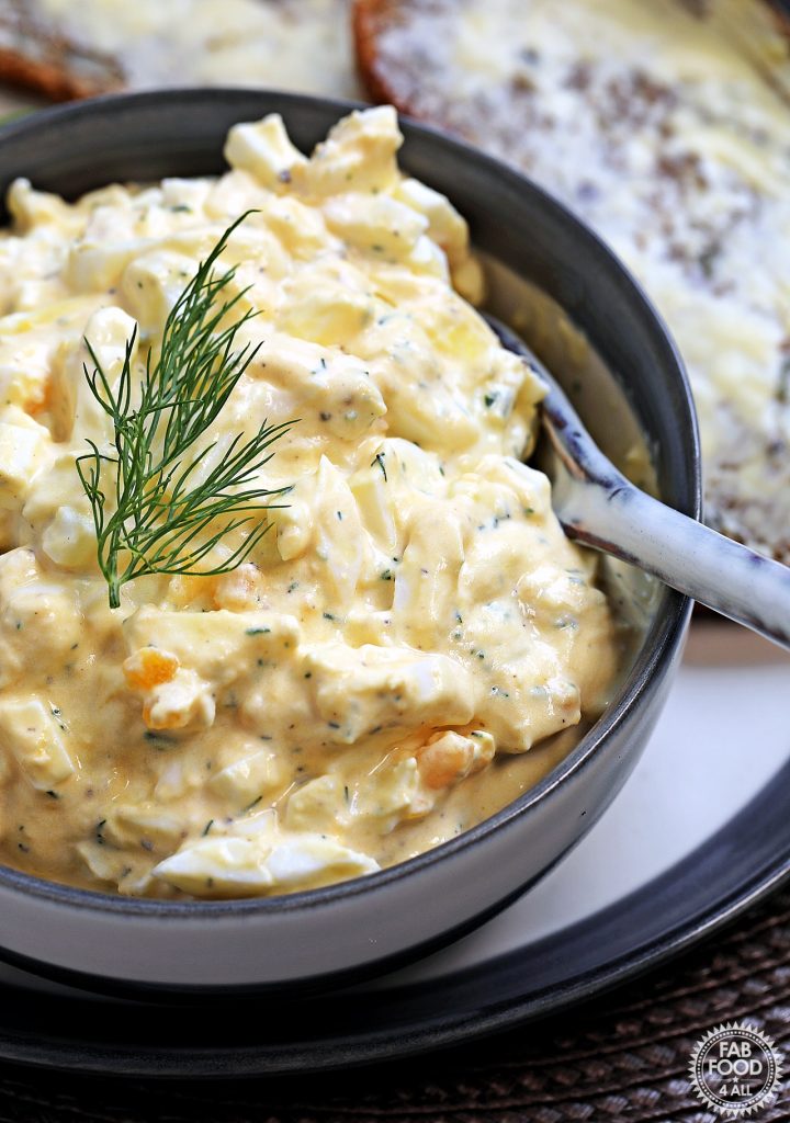 Close up of Healthy Egg Salad with Greek Yogurt (No Mayo) with a spoon in a bowl on a plate with buttered rye bread in the background.