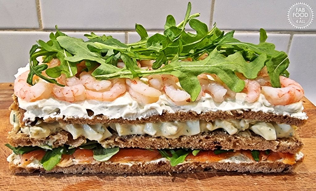 Smörgåstårta showing the inner layers (prawn, egg salad and smoked salmon) before the final slice of bread is added to the top and covered with cream cheese.