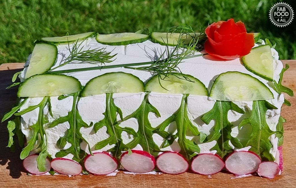 Smörgåstårta decorated in cream cheese, cucumber slices, rocket (arugula), radish slices, dill and a tomato rose.