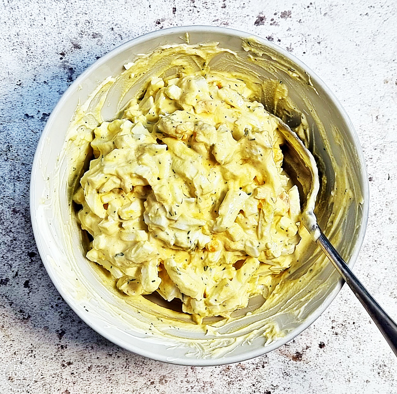Egg Salad with Greek Yogurt and dill in a bowl with a spoon after mixing.