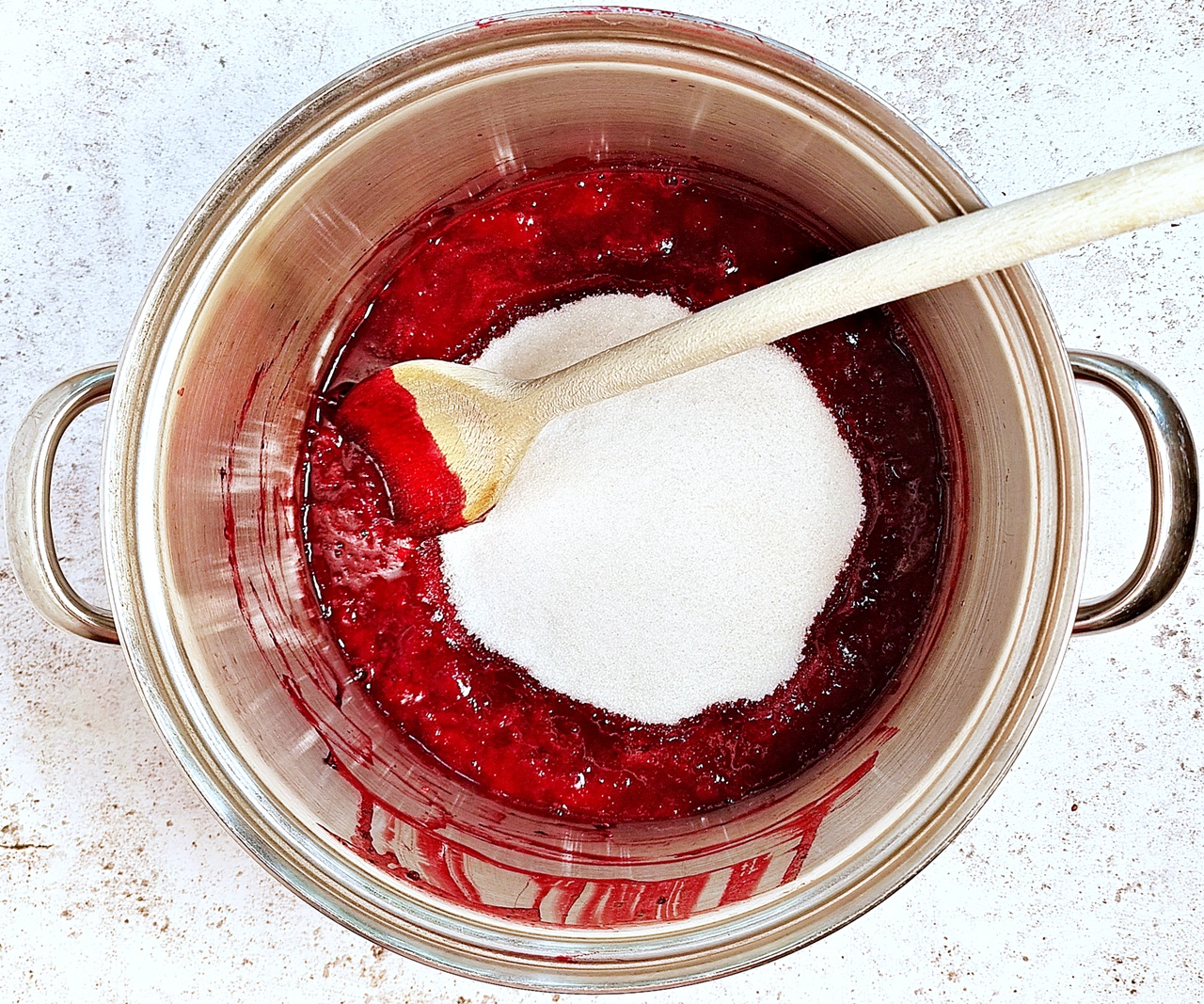 Stainless steel pot with cooked berry pulp/juice and granulated sugar added.