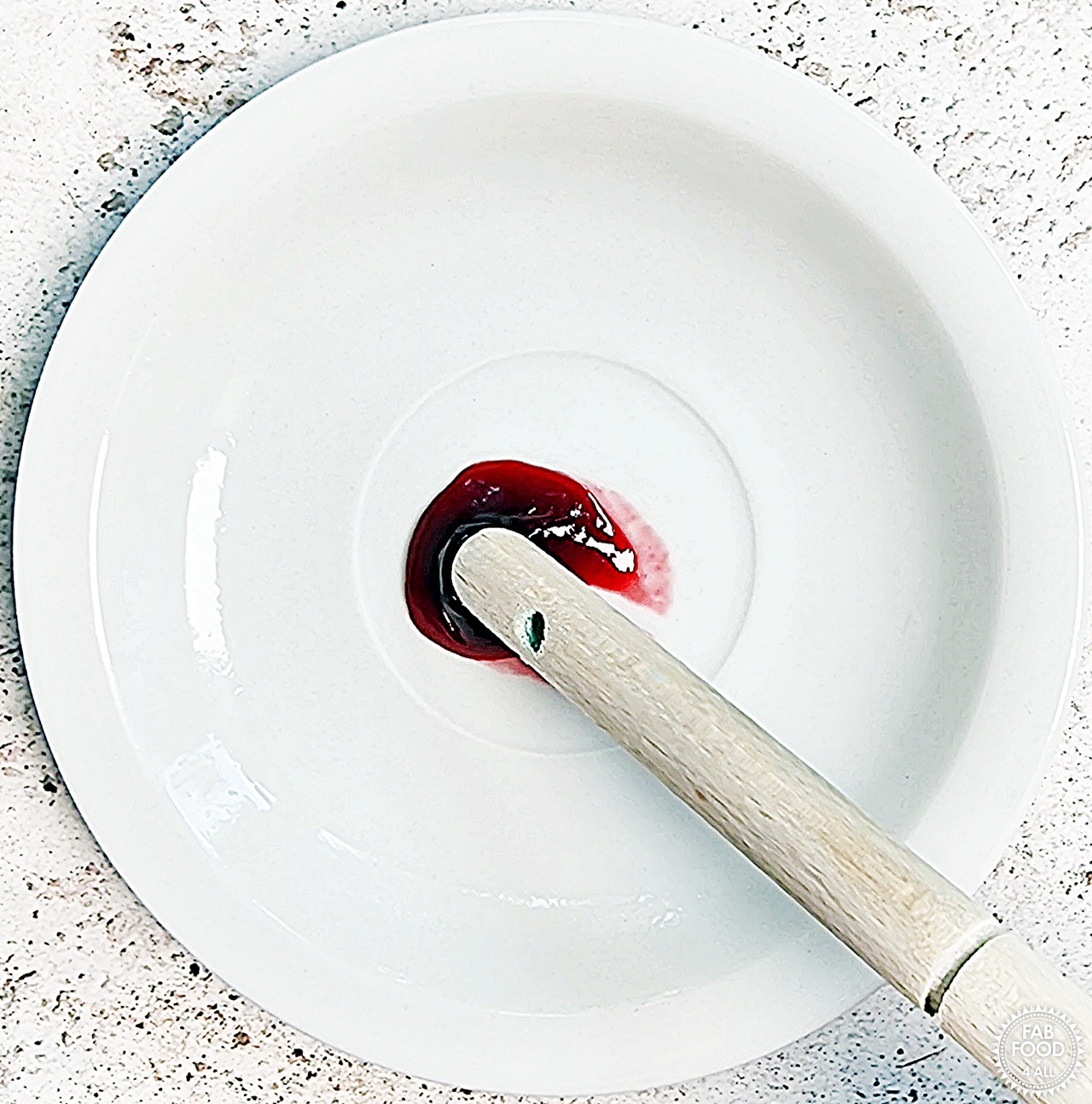 Chilled plate test showing a wooden spoon handle being pushed through a few drops of jam which crinkles when setting point is reached.